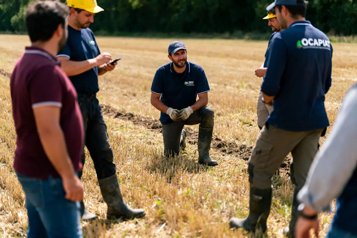 Des personnes discutent dans un champ, portant des tenues de travail et des bottes.